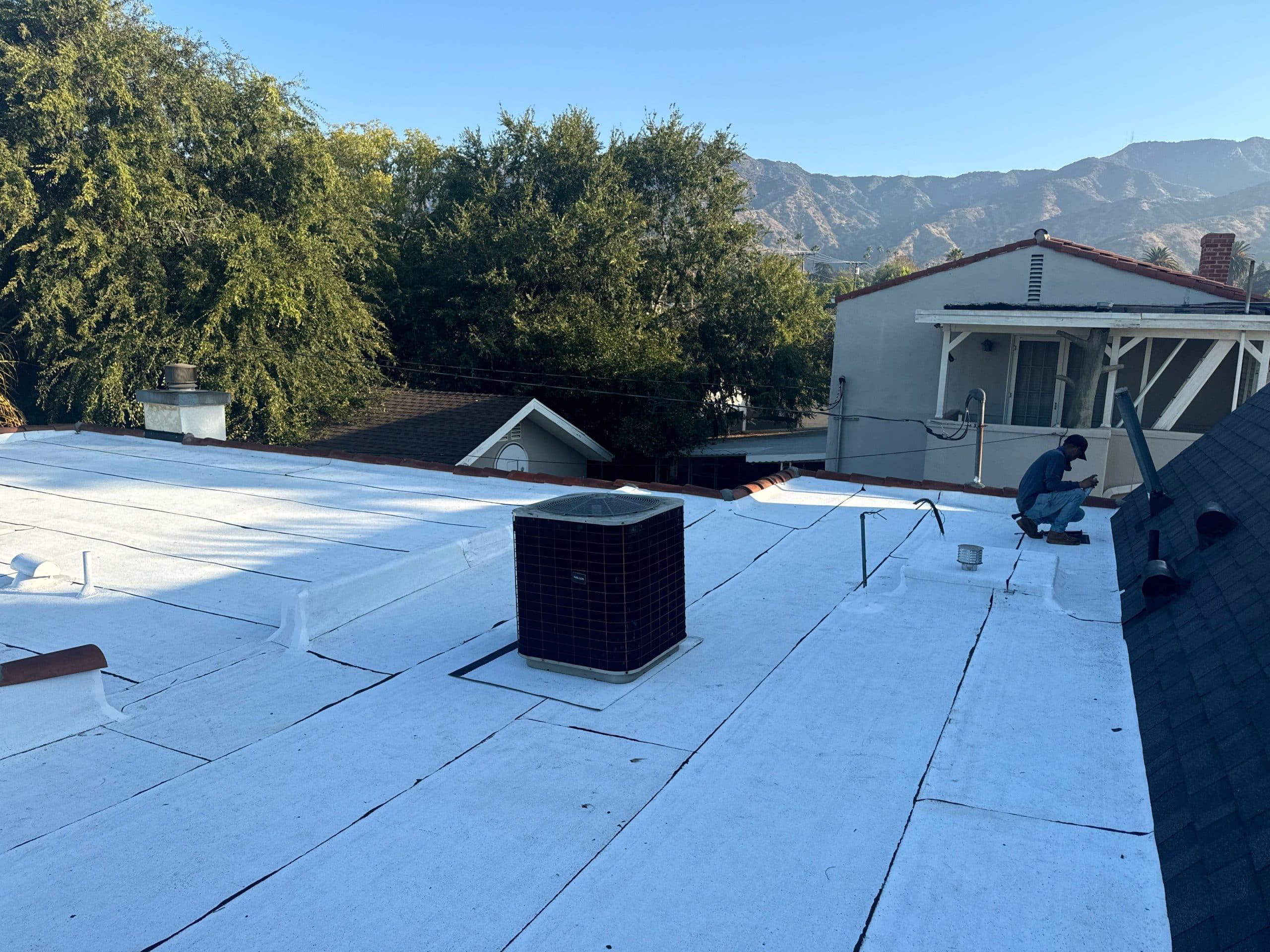 Worker repairing white flat roof with mountains behind