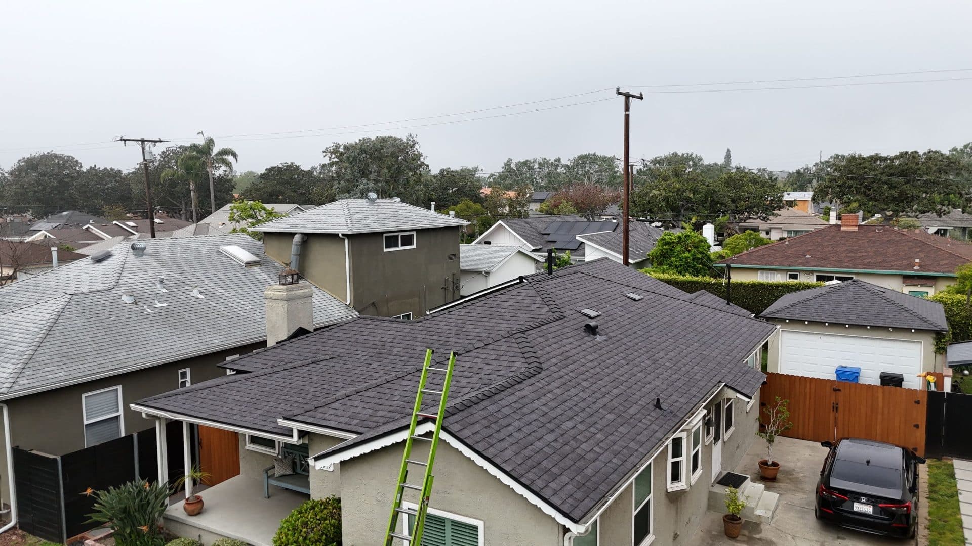 Completed dark asphalt shingle hip roof, green ladder leaning on eave — Roof Replacement Inc