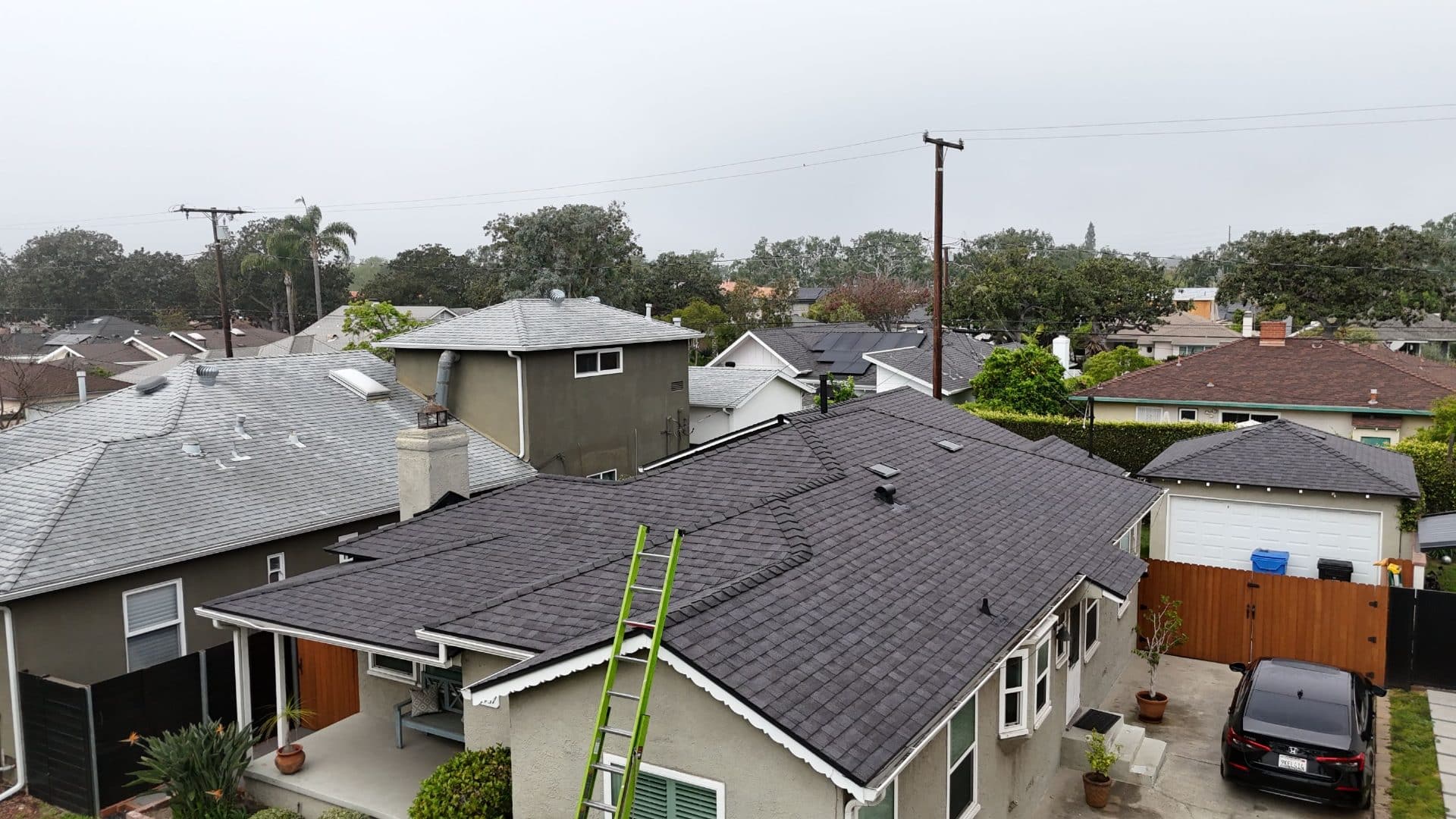Dark asphalt shingle reroof, hip roof, green ladder leaning on eave | Roof Replacement Inc Dark asphalt shingle reroof, hip roof, green ladder leaning on eave — Roof Replacement Inc