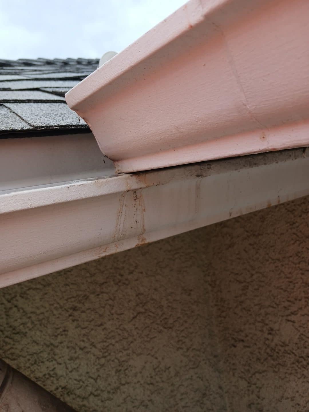 Pink fascia board, rain gutter, and asphalt shingles close-up — Roof Replacement Inc