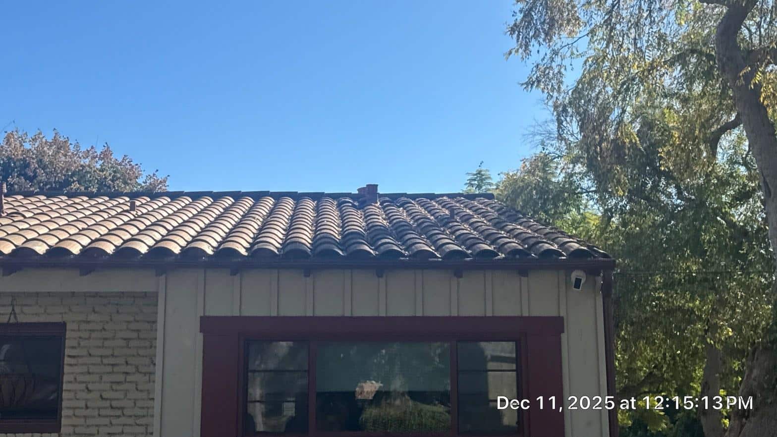 Spanish clay tile roof on stucco and brick home with gutters and security camera, sunny day.